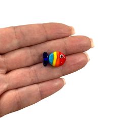 a hand holding two tiny colorful beads in it's left palm, one with an eye and the other with a fish