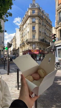 a person holding an open box with macaroons in it on a city street