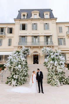 a bride and groom standing in front of a large building with white flowers on it