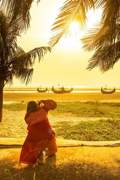 a woman sitting under a palm tree next to the ocean with boats in the background