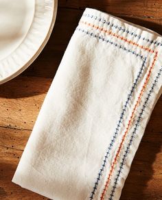 two folded towels sitting on top of a wooden table next to a plate and fork