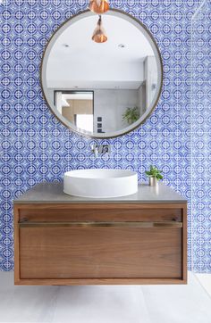 a bathroom with blue and white wallpaper and a round mirror on the wall above it