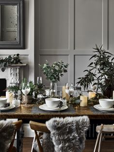 a dining room table set with plates, cups and saucers surrounded by greenery