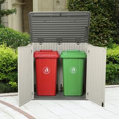 two red and green trash cans sitting in an outdoor storage area next to shrubbery