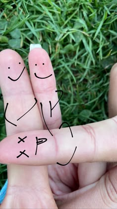 two fingers with faces drawn on them in front of some grass and one is holding the other