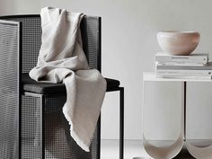 a chair with a blanket on top of it next to a white cabinet and vase