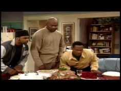 three men standing around a table with food on it and one man looking at the camera