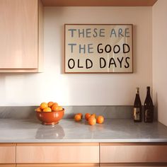 a bowl of oranges sitting on top of a counter next to bottles and a sign