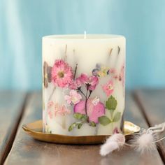 a white candle with pink flowers on it sitting on a wooden table next to a feather