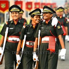 three women in uniforms are walking down the street together and smiling at the camera, with other people behind them