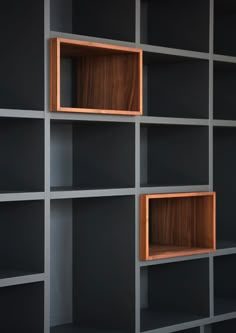 an empty bookcase with wooden shelves in the middle and dark grey walls behind it