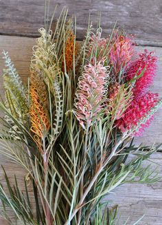 a bunch of flowers that are on top of a wooden table with some grass in it