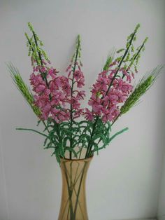 pink flowers are in a vase with green stems on a shelf next to a white wall