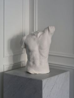 a white sculpture sitting on top of a marble block in front of a wall and floor