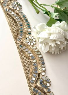 a white flower sitting next to a gold and blue bracelet on top of a table