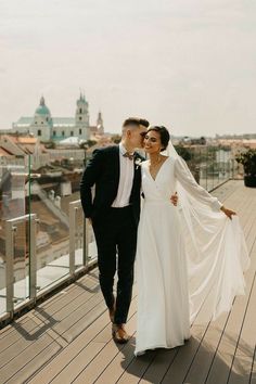 a bride and groom walking on a wooden deck in front of a cityscape