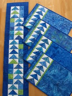 four quilted placemats on a wooden table with blue and green fabrics in the background