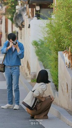 a woman kneeling down next to a man with a cat on his shoulder and another person holding a camera