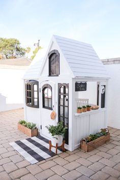 a small white house with potted plants on the outside