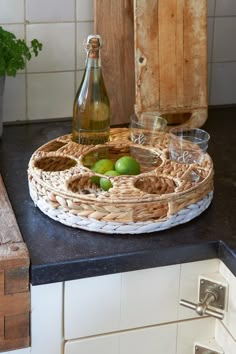 there is a bottle and some fruit on the counter in front of the glass bowl