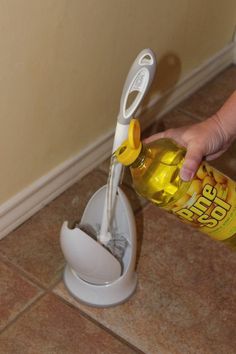 a person is holding a bottle in front of a toothbrush holder on the floor