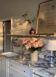 a marble counter top with flowers in a vase next to a sink and wine glasses