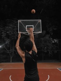 a young man is playing basketball on an outdoor court at night with the ball in the air