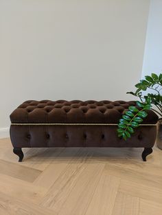 a brown bench sitting on top of a wooden floor next to a potted plant