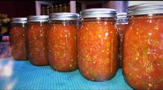 several jars filled with pickles sitting on top of a blue tablecloth covered counter