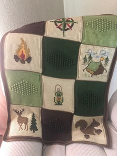 a crocheted blanket with animals and trees on it is sitting on a chair