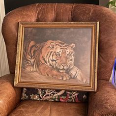 a painting of a tiger laying on top of a brown chair next to a blue vase