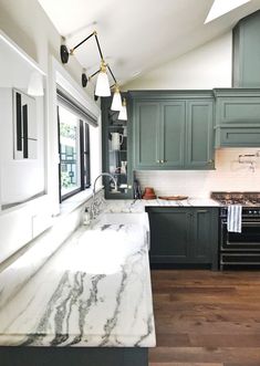 a kitchen with green cabinets and marble counter tops, along with an island in the middle