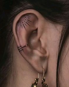 a woman with black and white tattoos on her face, behind the ear is a pair of gold - plated earrings