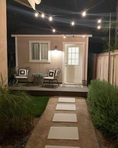 a small house is lit up at night with string lights on the front door and patio