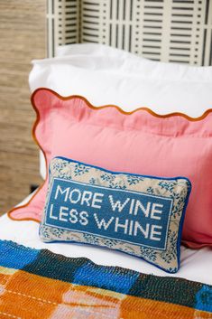 a pillow that says more wine less whine on it sitting on top of a bed