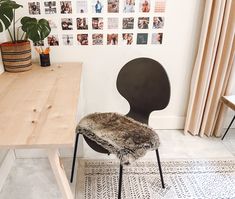 a chair with a furry seat pad sitting in front of a wooden table and pictures on the wall