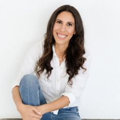 a woman sitting on the floor with her legs crossed and looking at the camera while smiling