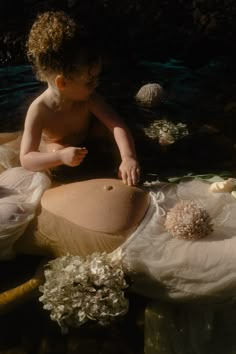 a young child sitting on top of a body of water next to shells and flowers