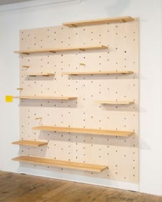 a wall mounted shelf with wooden shelves and pegs on the sides in an empty room