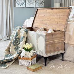 an open trunk sitting on the floor next to a basket with flowers and blankets in it