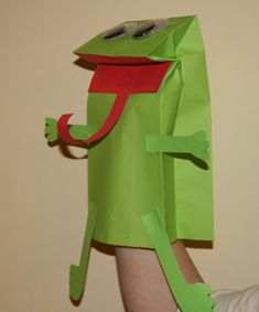 a person holding up a green paper bag with a frog on it's head