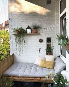 a couch sitting on top of a wooden bench next to a white brick wall with potted plants