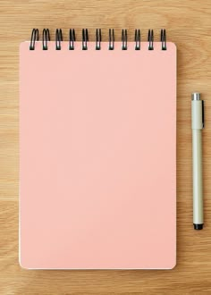 a pink notebook with black spirals and a pen next to it on a wooden surface