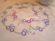 a white table cloth with purple and blue flowers on it, next to a bowl