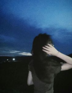 a woman standing in the dark with her hands on her head and looking at the sky