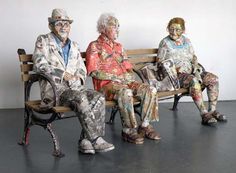 three people are sitting on a bench covered in paper mache and painted with different colors