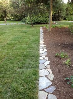 a stone path in the middle of a grassy area next to a tree and shrubbery