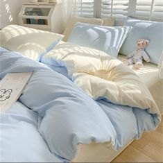 a bed with blue and white sheets, pillows and a teddy bear sitting on it