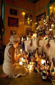 a woman sitting on the floor in front of a wall full of bottles and candles