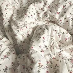 an unmade bed with white and red flowers on it's comforter cover